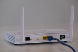 A person plugs an Ethernet cable into a laptop while a Wi-Fi router sits nearby on a desk.