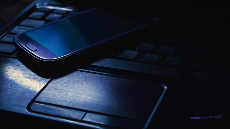 Person using a laptop at a public table while checking Wi-Fi security settings on a smartphone.