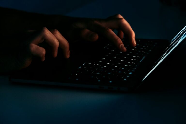 Person examining a suspicious email on a laptop beside a smartphone and handwritten notes.